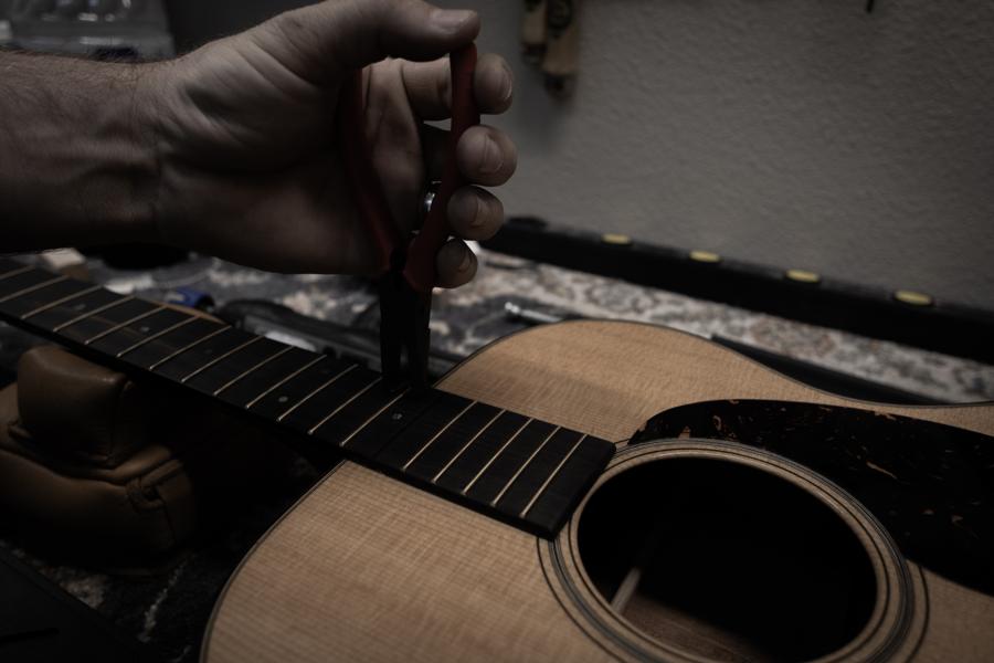 Tech's hands at work on the fretboard of an acoustic guitar